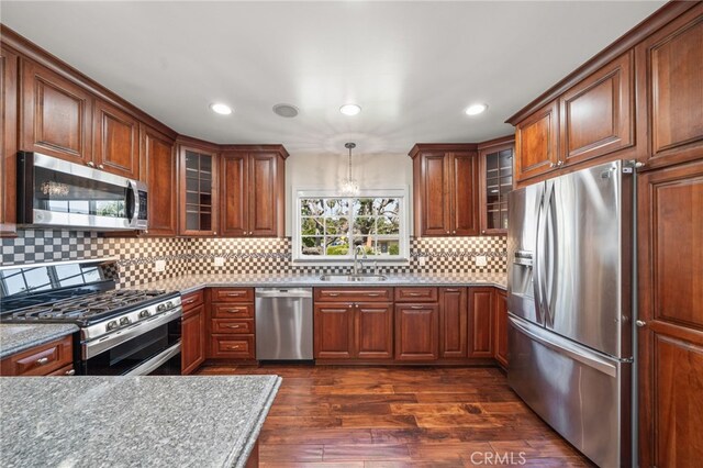 kitchen with tasteful backsplash, dark wood-style flooring, brown cabinetry, stainless steel appliances, and a sink