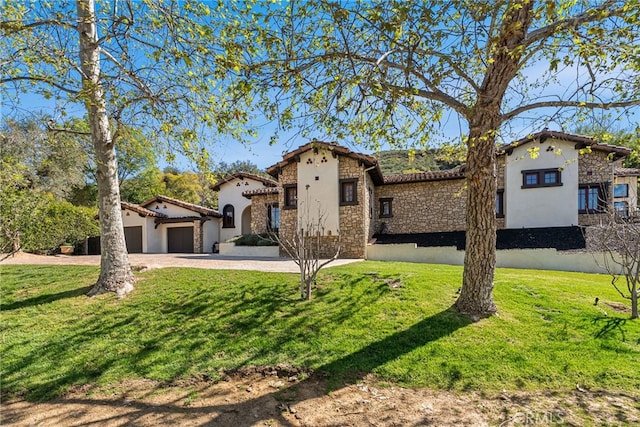 mediterranean / spanish house featuring a front lawn, driveway, stone siding, and a garage