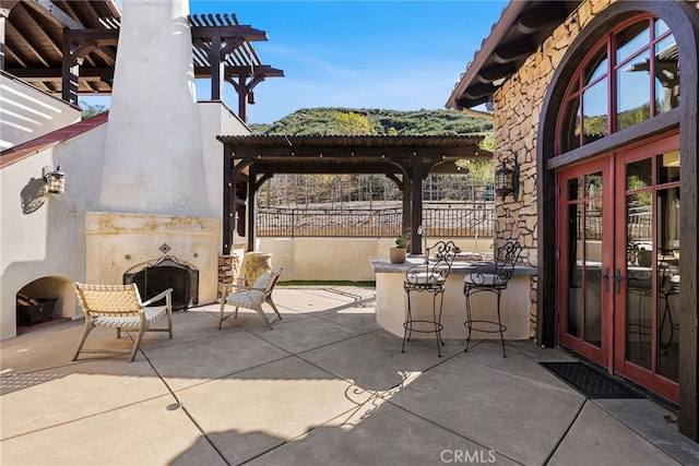 view of patio featuring french doors, an outdoor fireplace, and a pergola