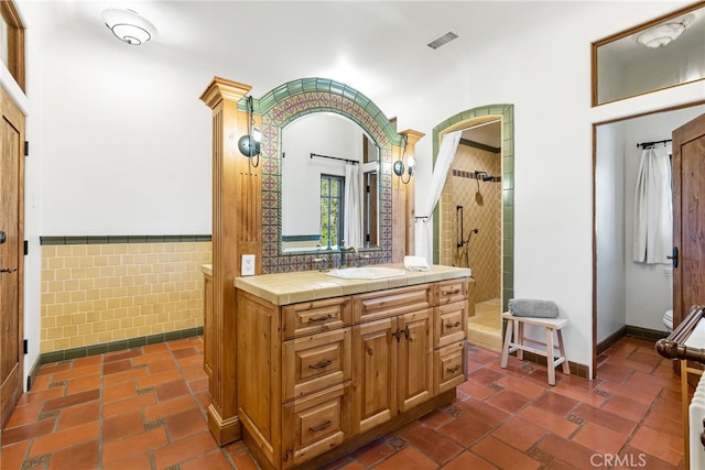 bathroom with tile walls, visible vents, a tile shower, toilet, and vanity