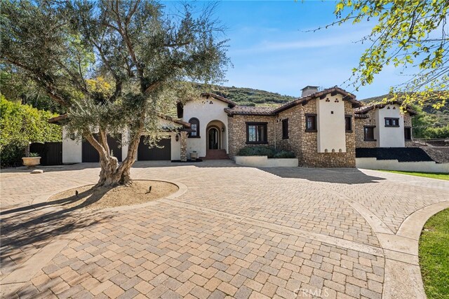 mediterranean / spanish-style home featuring stone siding, curved driveway, a garage, and stucco siding