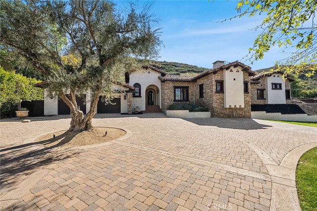 mediterranean / spanish home with stone siding, a garage, curved driveway, and stucco siding