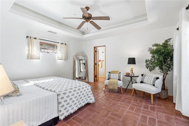 bedroom featuring a tray ceiling, brick floor, ceiling fan, and visible vents