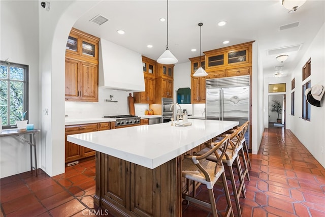 kitchen featuring light countertops, visible vents, custom exhaust hood, and a center island with sink