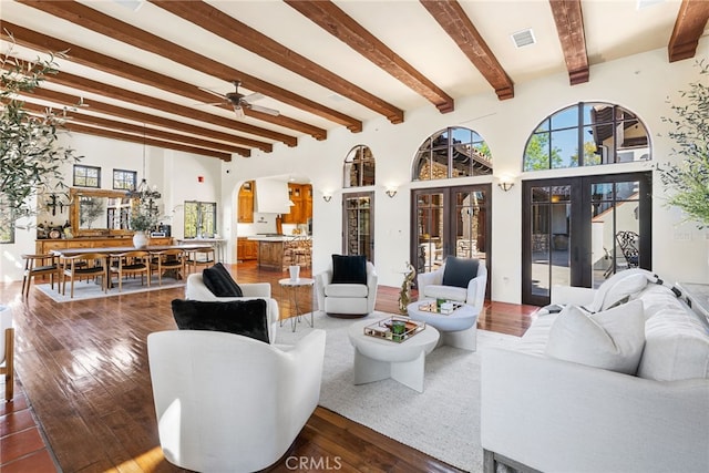 living area with arched walkways, dark wood-style flooring, ceiling fan, and beamed ceiling