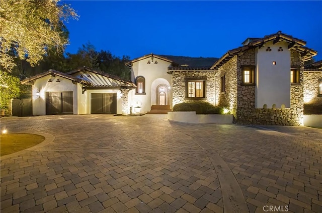 mediterranean / spanish-style house featuring curved driveway, stucco siding, an attached garage, stone siding, and a tiled roof