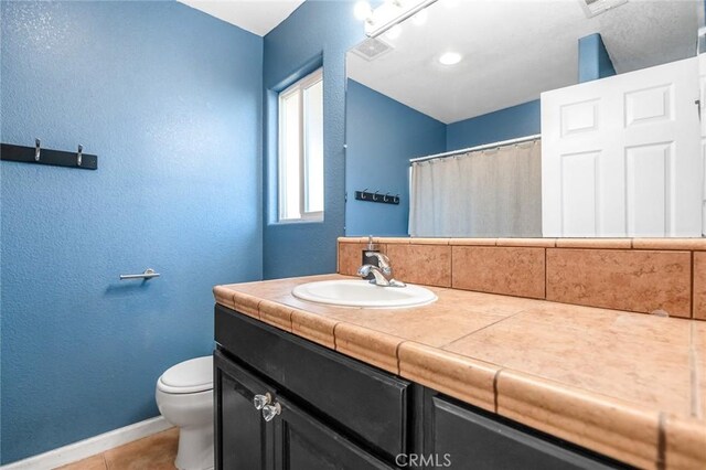 full bath with tile patterned floors, toilet, baseboards, vanity, and a textured wall