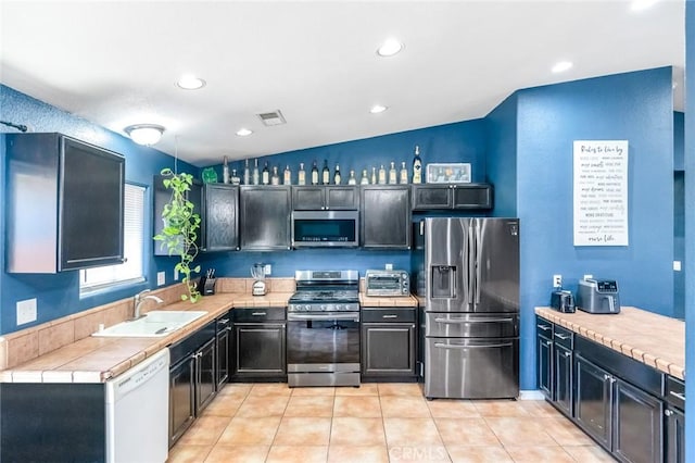 kitchen featuring visible vents, tile countertops, light tile patterned floors, appliances with stainless steel finishes, and a sink
