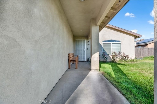 doorway to property with a patio area, stucco siding, a lawn, and fence