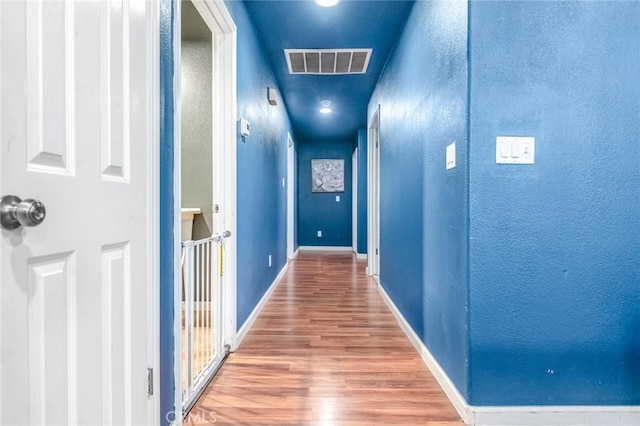 corridor featuring visible vents, baseboards, wood finished floors, and a textured wall