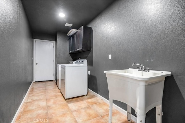 clothes washing area featuring baseboards, a textured wall, light tile patterned flooring, cabinet space, and separate washer and dryer