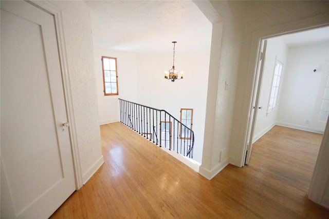 hallway featuring baseboards, a notable chandelier, wood finished floors, and an upstairs landing