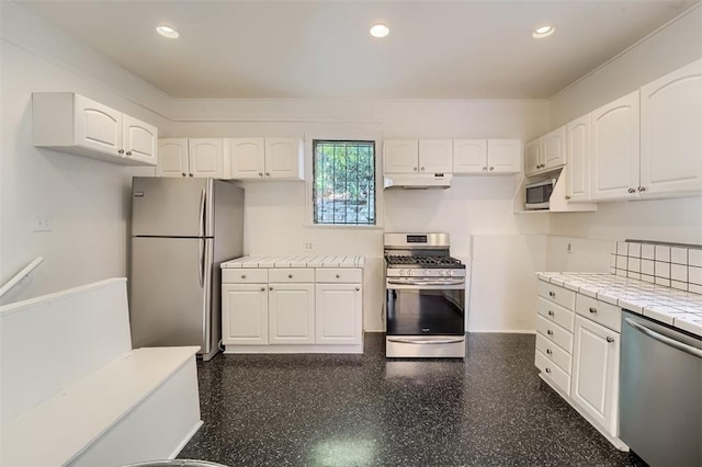 kitchen featuring tile counters, recessed lighting, under cabinet range hood, stainless steel appliances, and white cabinetry