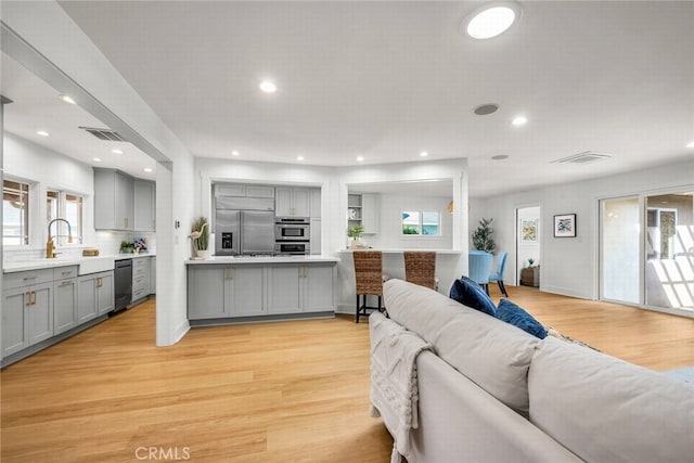 kitchen featuring open floor plan, light wood-style flooring, gray cabinets, and stainless steel appliances