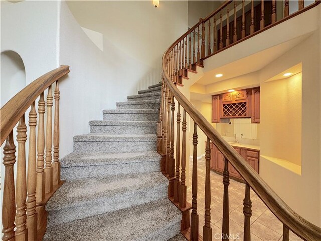 stairway with recessed lighting, wet bar, tile patterned flooring, and a towering ceiling