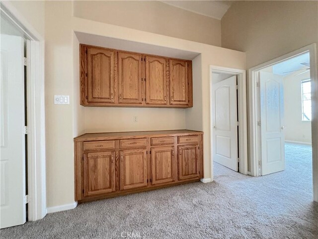 interior space with baseboards, light carpet, and brown cabinets