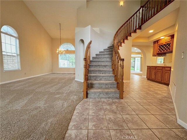 staircase featuring a towering ceiling, arched walkways, baseboards, tile patterned floors, and an inviting chandelier
