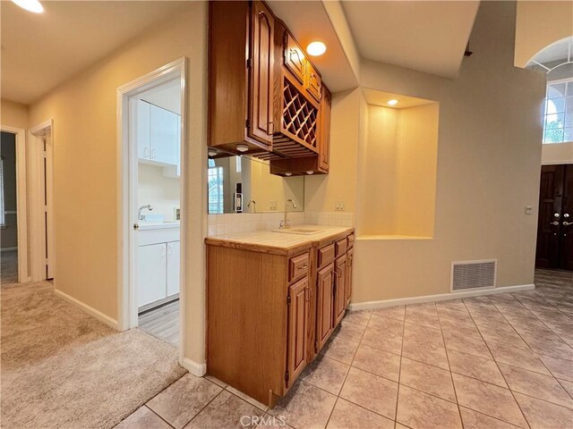 kitchen featuring tile countertops, visible vents, brown cabinets, a sink, and light tile patterned flooring