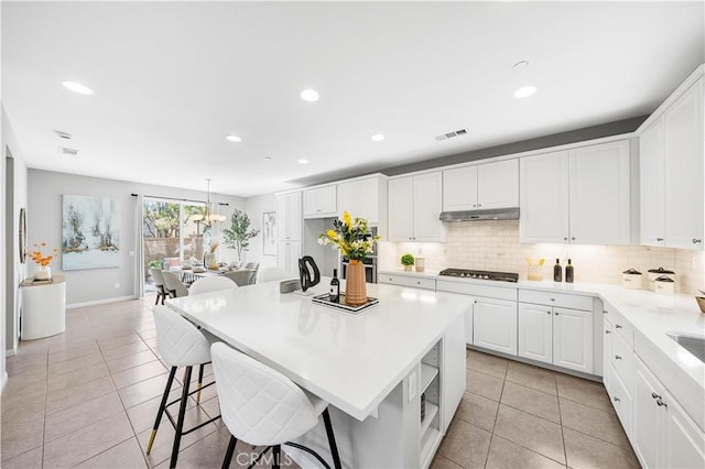kitchen featuring under cabinet range hood, visible vents, backsplash, and light tile patterned flooring