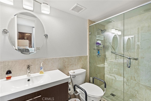 bathroom featuring vanity, tile walls, toilet, a shower stall, and visible vents