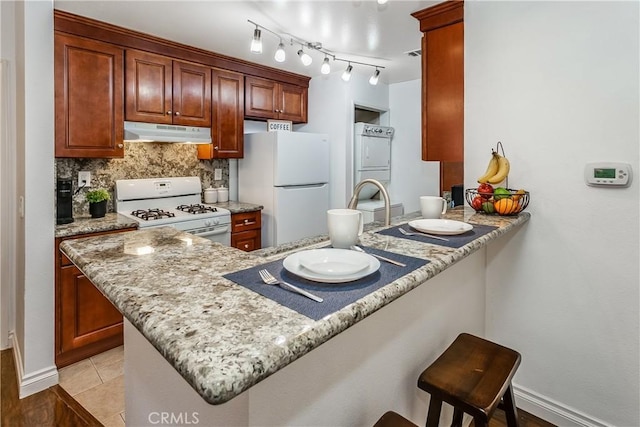 2304 Archwood Ln Unit 98, Simi Valley, CA 93063 - kitchen with white appliances, under cabinet range hood, stacked washing machine and dryer, a peninsula, and decorative backsplash