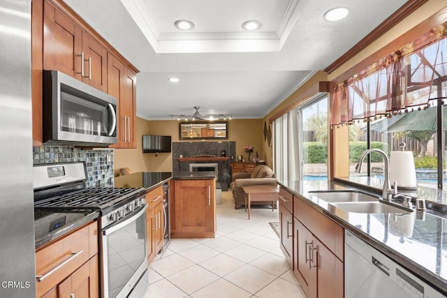 kitchen with ornamental molding, appliances with stainless steel finishes, dark stone counters, and a sink