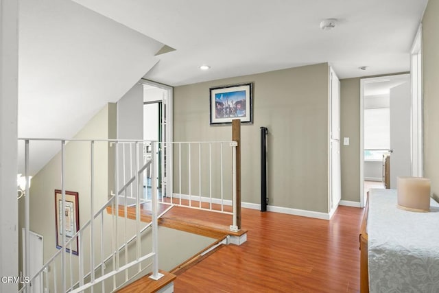 hallway featuring wood finished floors, an upstairs landing, and baseboards