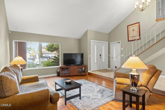 living area with baseboards, stairs, an inviting chandelier, wood finished floors, and high vaulted ceiling