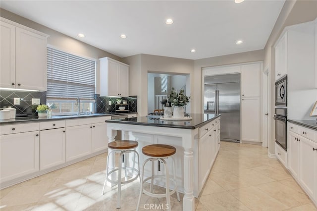 kitchen with built in appliances, a kitchen island, dark countertops, tasteful backsplash, and a sink