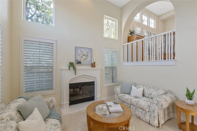 living room featuring arched walkways, a glass covered fireplace, a towering ceiling, and tile patterned floors
