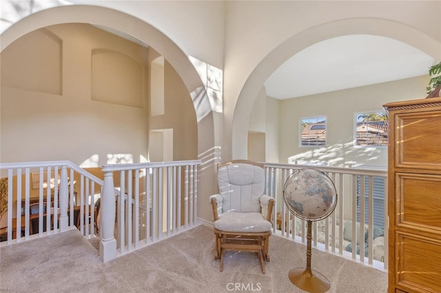 sitting room featuring arched walkways, carpet, and an upstairs landing