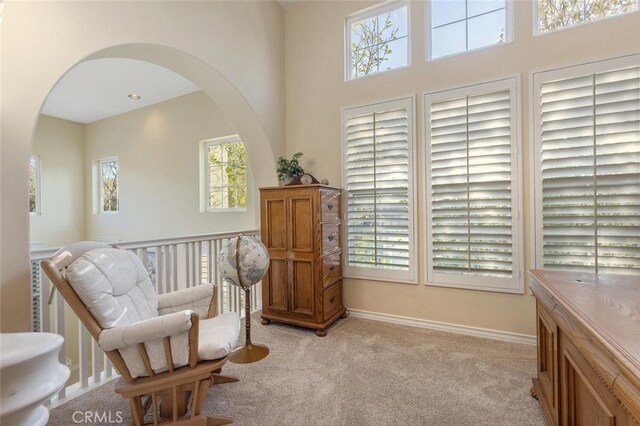 living area with arched walkways, baseboards, a towering ceiling, and light colored carpet