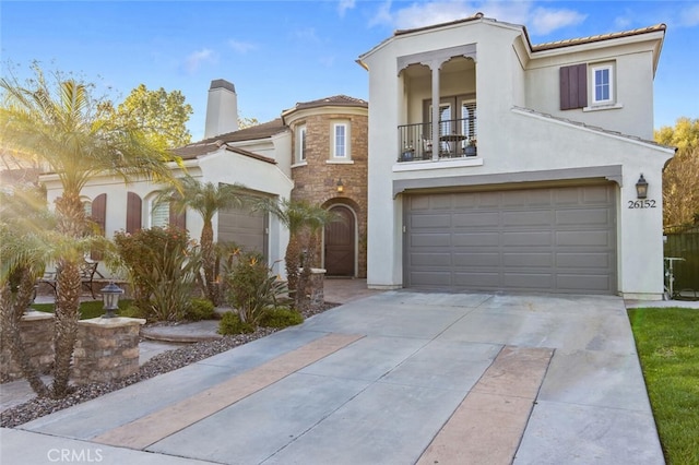 mediterranean / spanish-style house with stucco siding, a balcony, a chimney, and concrete driveway