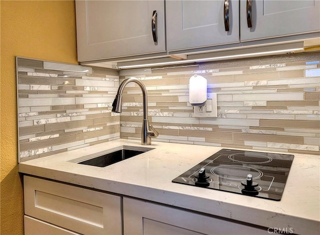 24055 Paseo Del Lago W Unit 1455, Laguna Woods, CA 92637 - kitchen featuring black electric cooktop, tasteful backsplash, a sink, light stone counters, and gray cabinetry