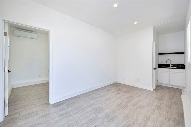 interior space with recessed lighting, a wall mounted air conditioner, light wood finished floors, a sink, and baseboards