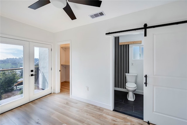 unfurnished bedroom featuring a barn door, light wood-type flooring, visible vents, and french doors