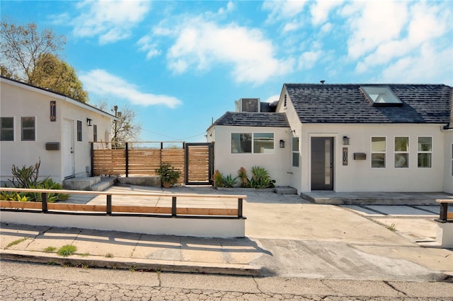view of front facade featuring fence, roof with shingles, and stucco siding