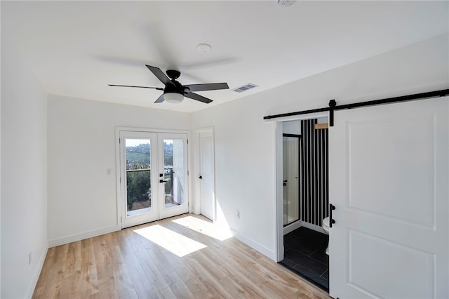 empty room featuring a barn door, visible vents, a ceiling fan, french doors, and light wood-style flooring