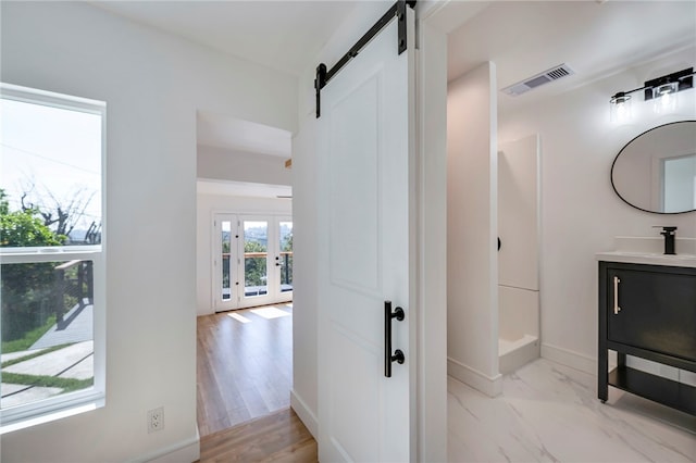 hall with a barn door, visible vents, a sink, french doors, and baseboards