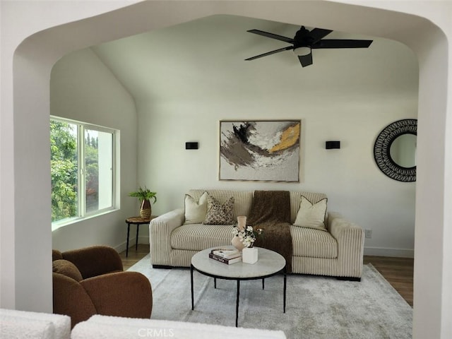 living area featuring wood finished floors, ceiling fan, arched walkways, baseboards, and lofted ceiling
