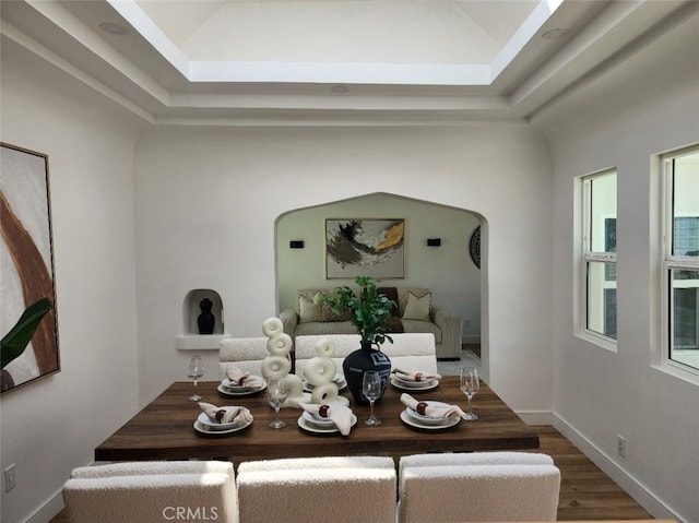 dining space with lofted ceiling, baseboards, wood finished floors, and arched walkways