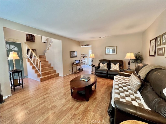 living area with baseboards, light wood-style flooring, and stairs