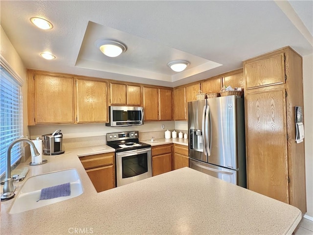 kitchen featuring light countertops, a tray ceiling, appliances with stainless steel finishes, and a sink