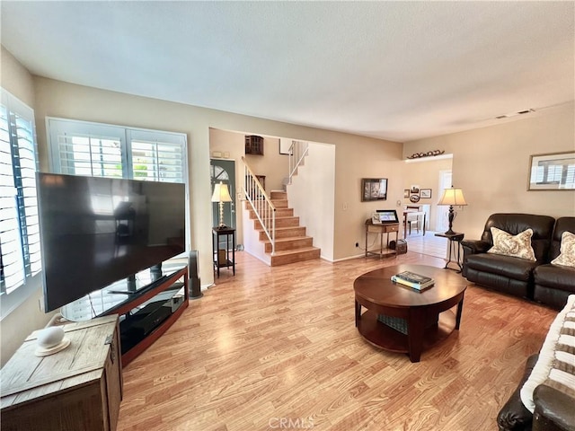 living area with light wood-type flooring, stairs, baseboards, and a wealth of natural light