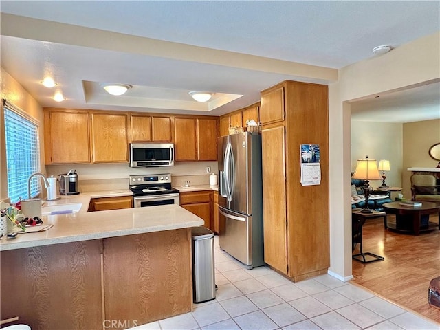 kitchen with light countertops, a tray ceiling, a sink, light tile patterned floors, and stainless steel appliances