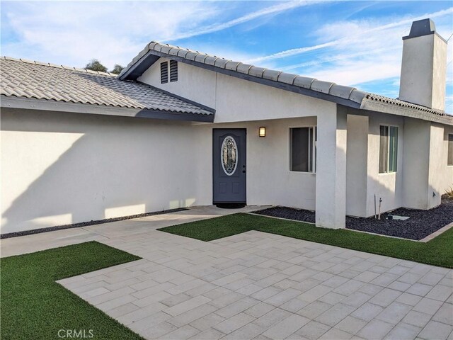 property entrance featuring stucco siding, a chimney, and a patio