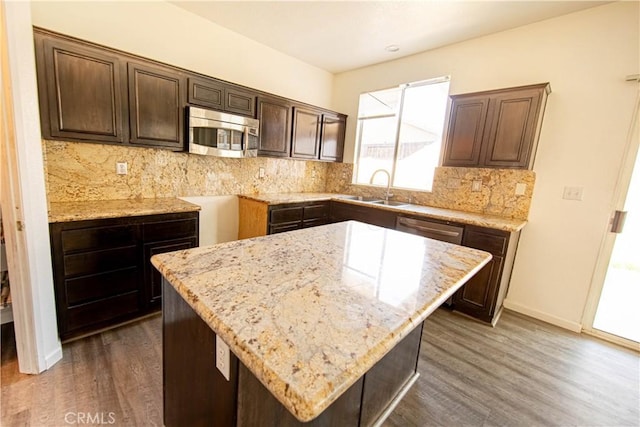 kitchen with dark brown cabinetry, light stone countertops, stainless steel appliances, and a sink