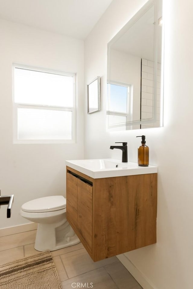 bathroom with tile patterned flooring, toilet, vanity, and a healthy amount of sunlight