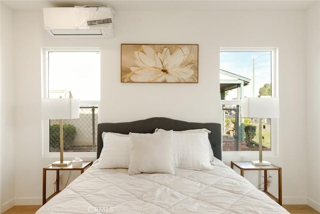 bedroom featuring an AC wall unit, baseboards, and wood finished floors