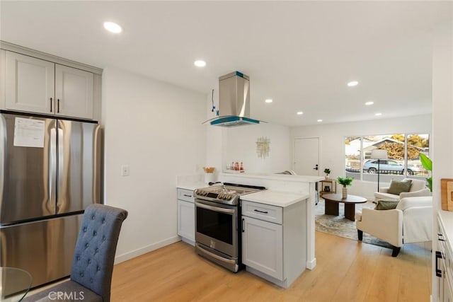 kitchen featuring light countertops, light wood-style flooring, a peninsula, island range hood, and stainless steel appliances